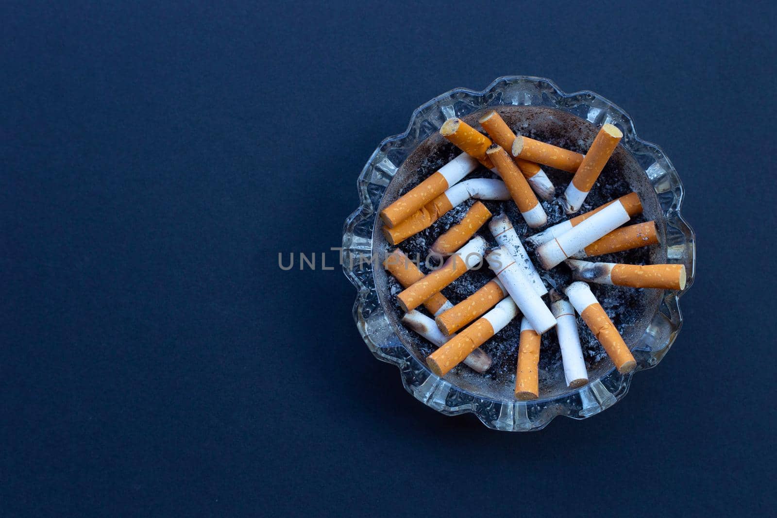 Cigarette butts in glass ashtray on dark background.