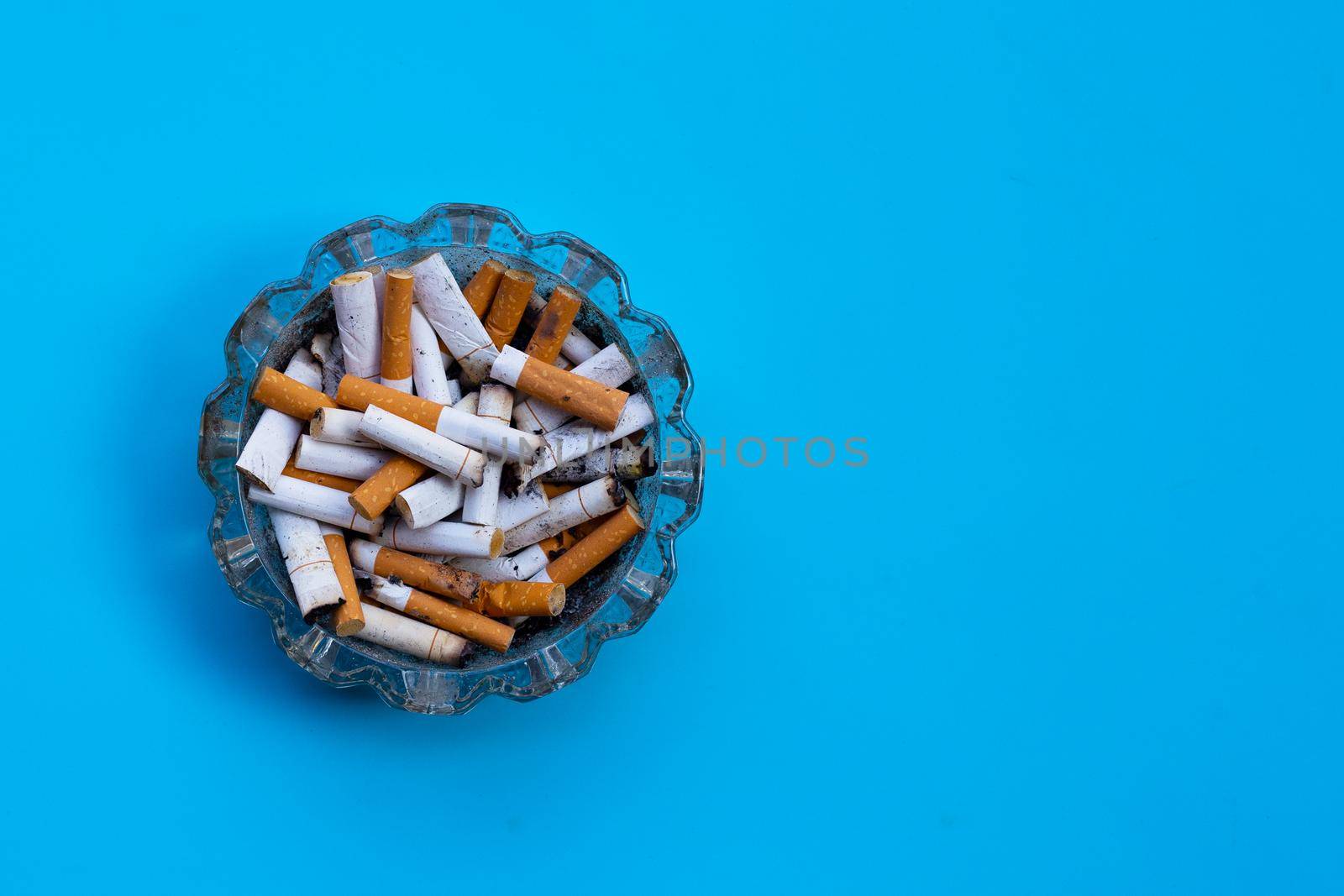 Cigarette butts in glass ashtray on blue background.