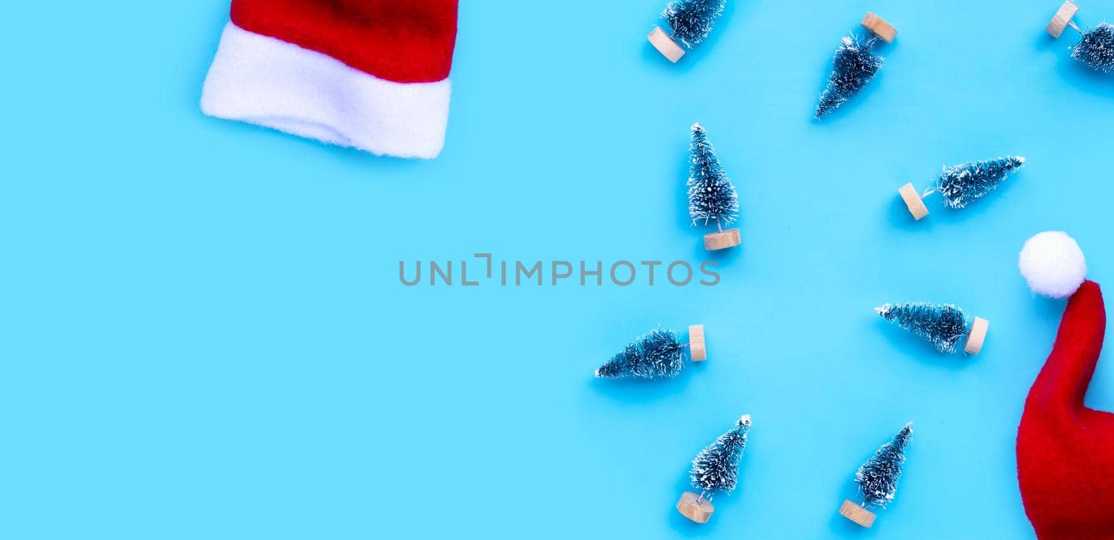Santa hats with miniature christmas pine tree on blue background. by Bowonpat