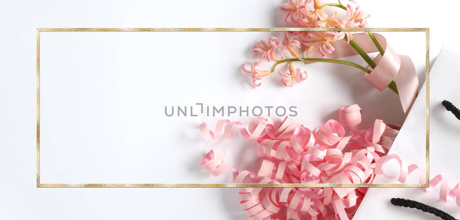 Pink spring flowers, pink gift streamer in white gift bag on white background. Beautiful spring card for Birthday, Woman, Valentines, Mothers Day in pastel colours. Horizontal flat lay. Copy space