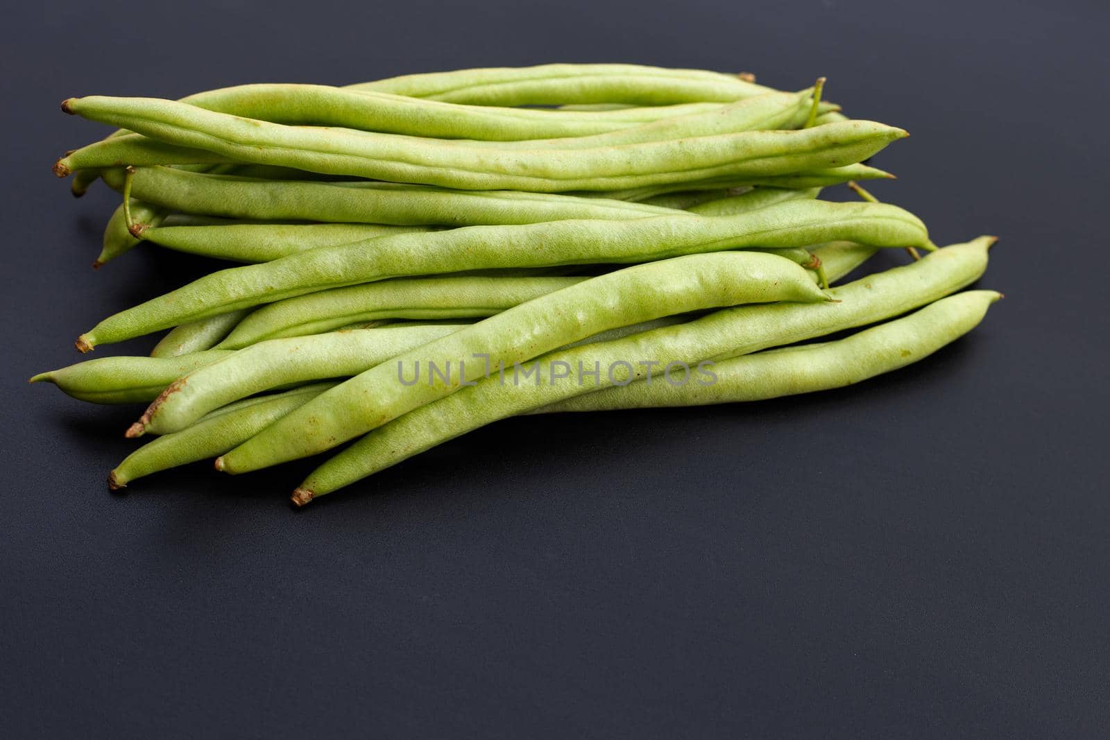 Pile of green bean pods on dark background.