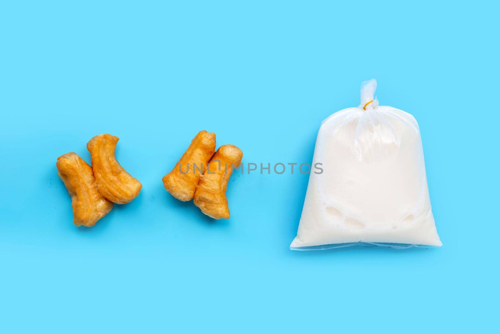 Soymilk in plastic bag with deep-fried dough stick or chinese bread stick on blue background. Top view