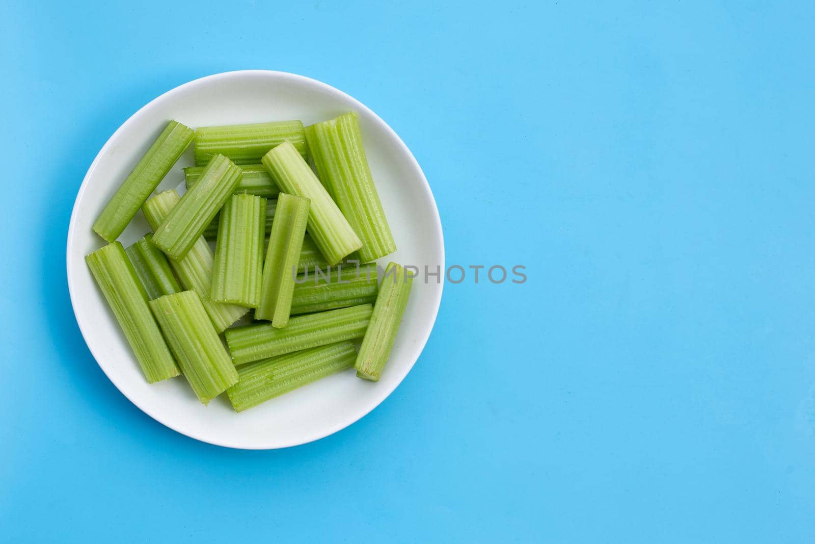 Fresh celery in white plate on blue background. Copy space