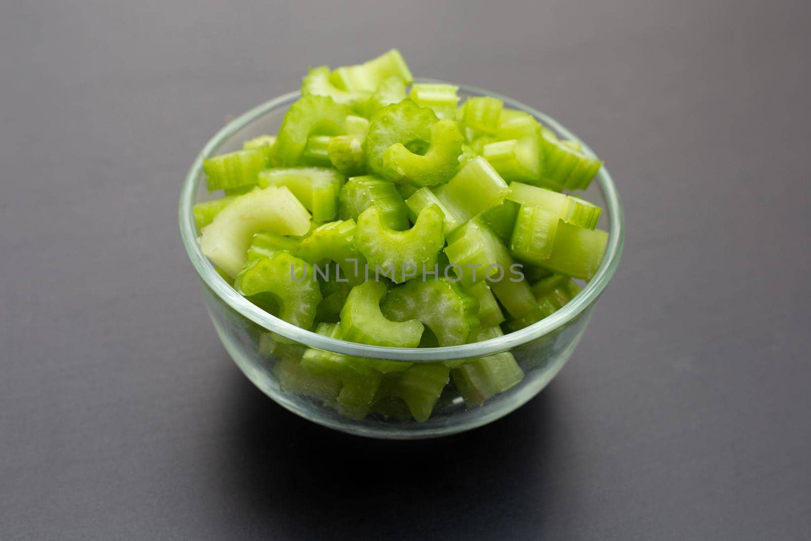Fresh celery slices in glass bowl on dark background. 