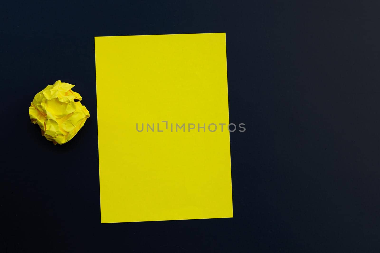 Yellow sheet with crumpled paper ball on dark background. Copy space