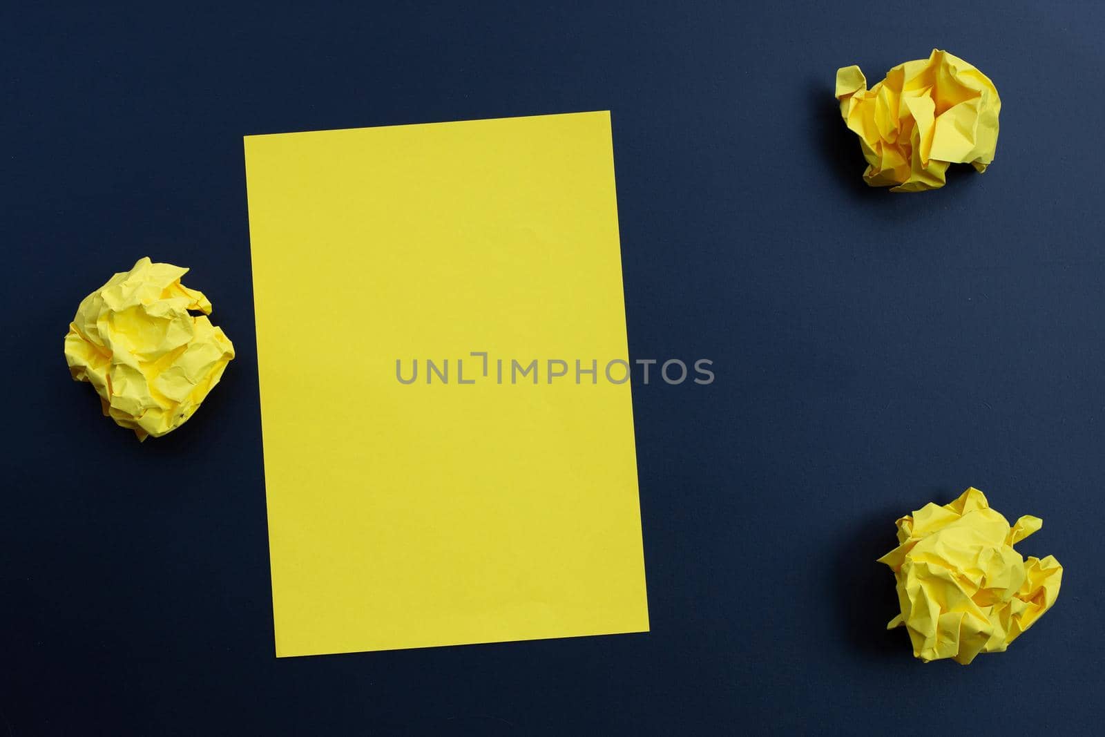 Yellow sheet with crumpled paper balls on dark background. Copy space