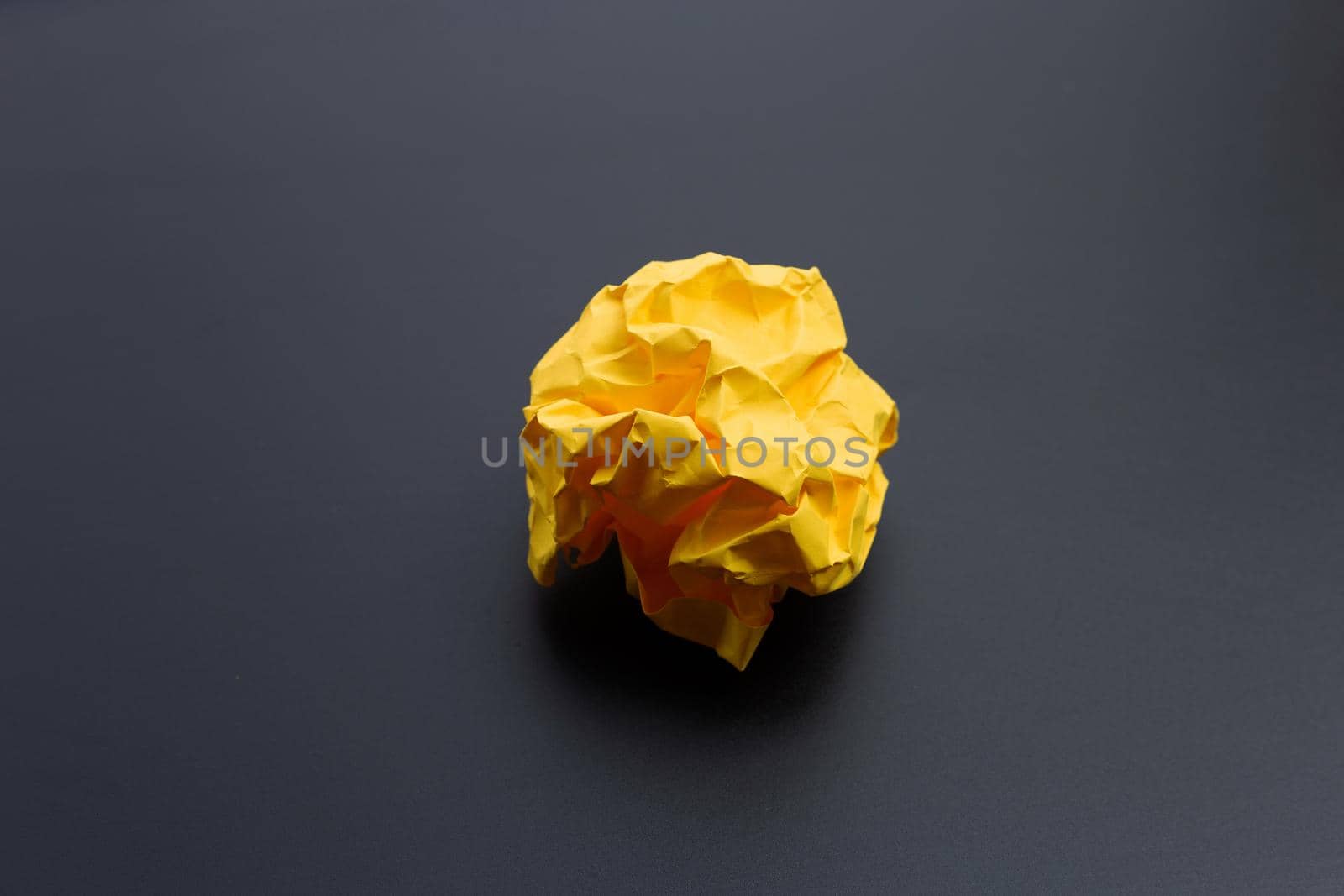 Crumpled yellow paper ball on dark background. Copy space