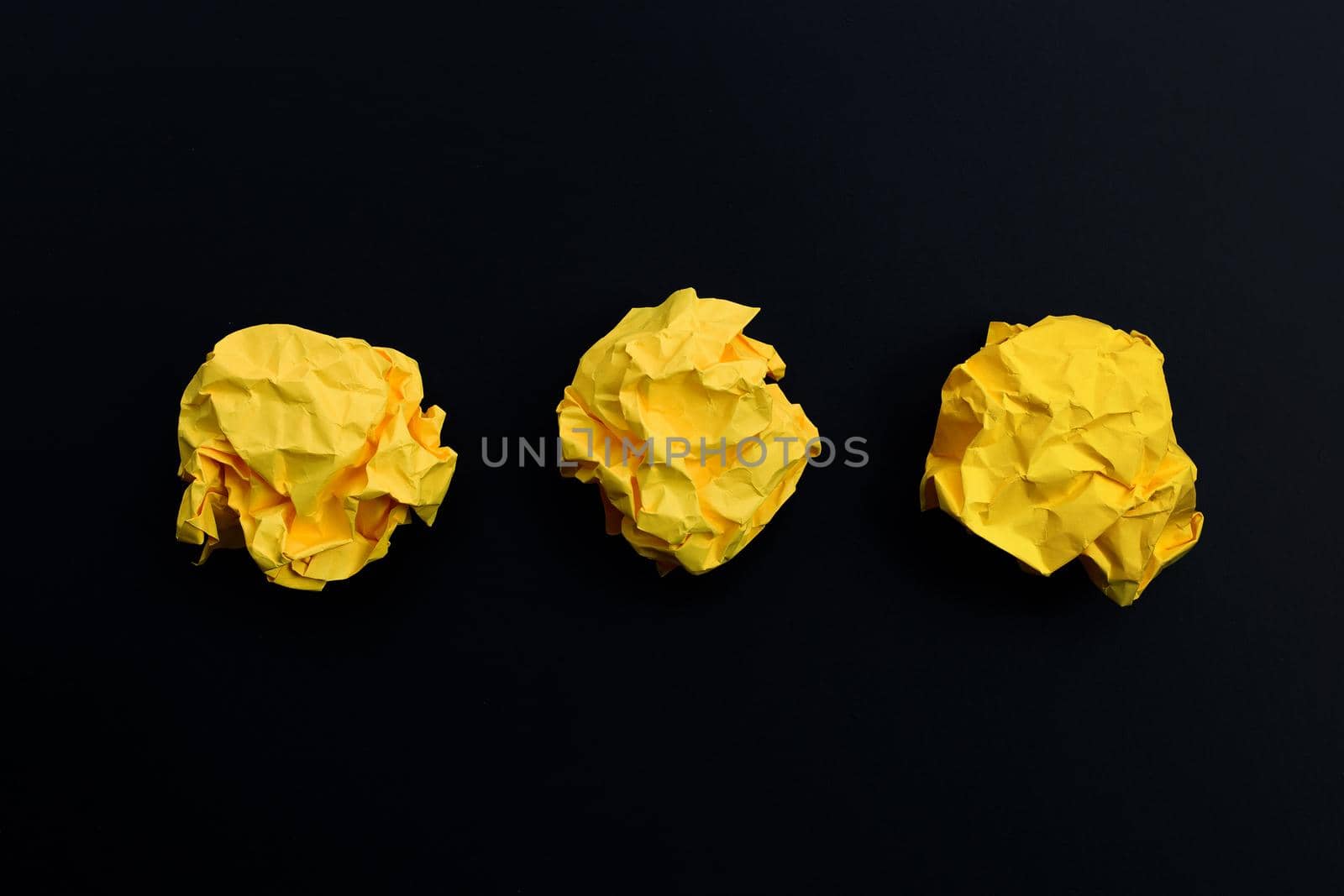 Crumpled yellow paper balls on dark background. Copy space