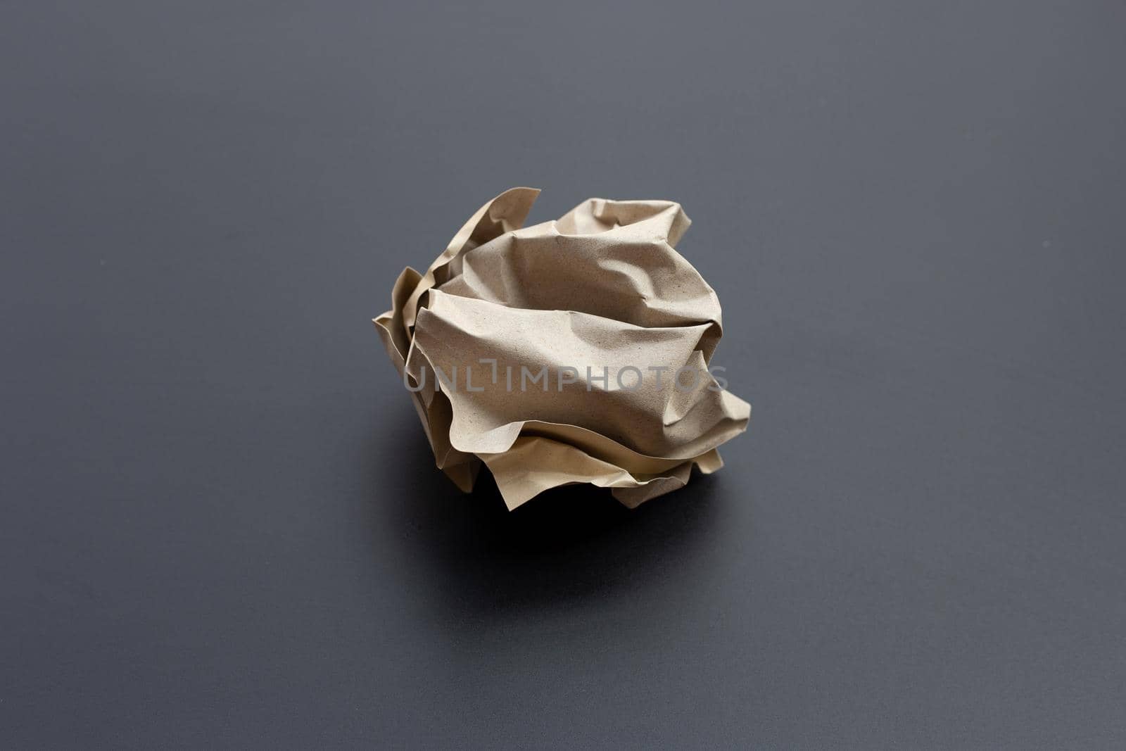 Crumpled brown paper ball on dark background. Copy space