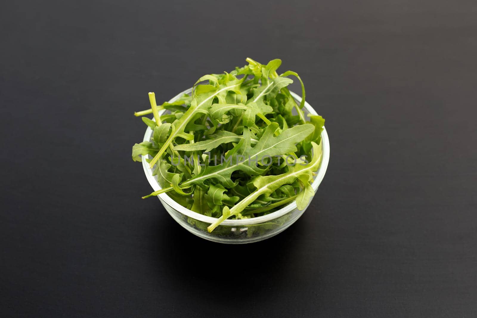 Fresh green rocket salad in glass bowl on dark background.