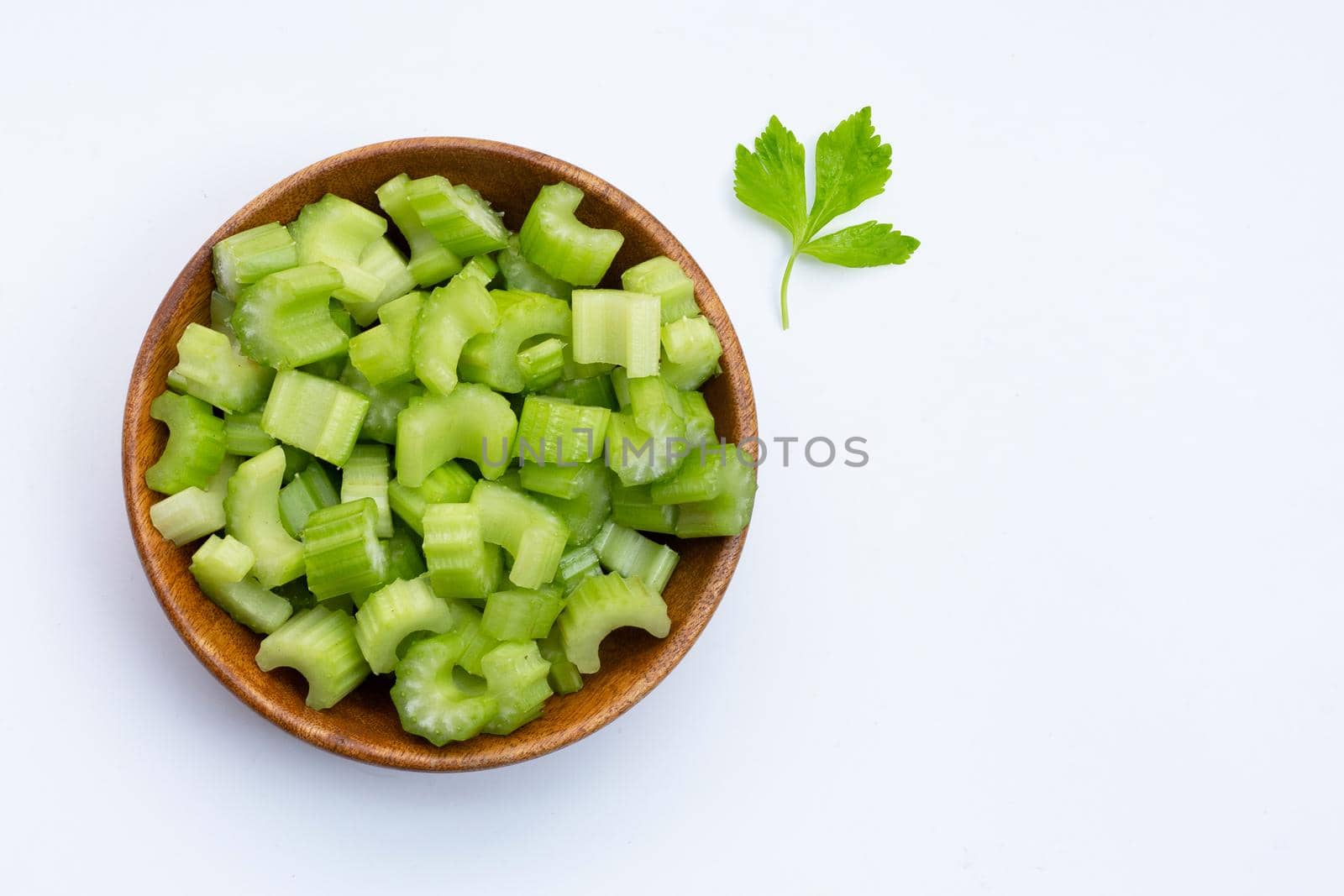 Fresh celery slices in wooden bowl on white background. Copy space