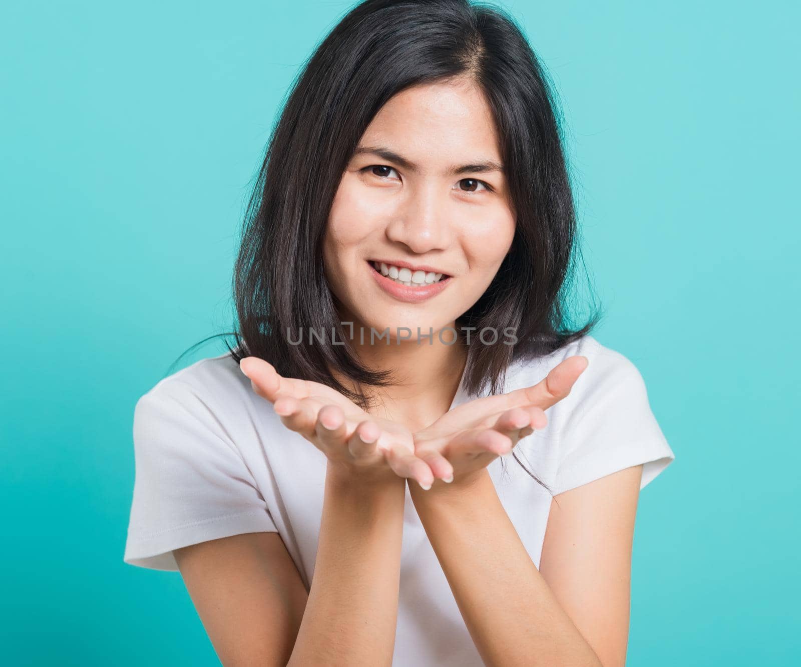 Portrait happy Asian beautiful young woman smile standing wear a white t-shirt, She blowing air kiss something on palms, studio shot on blue background with copy space for text