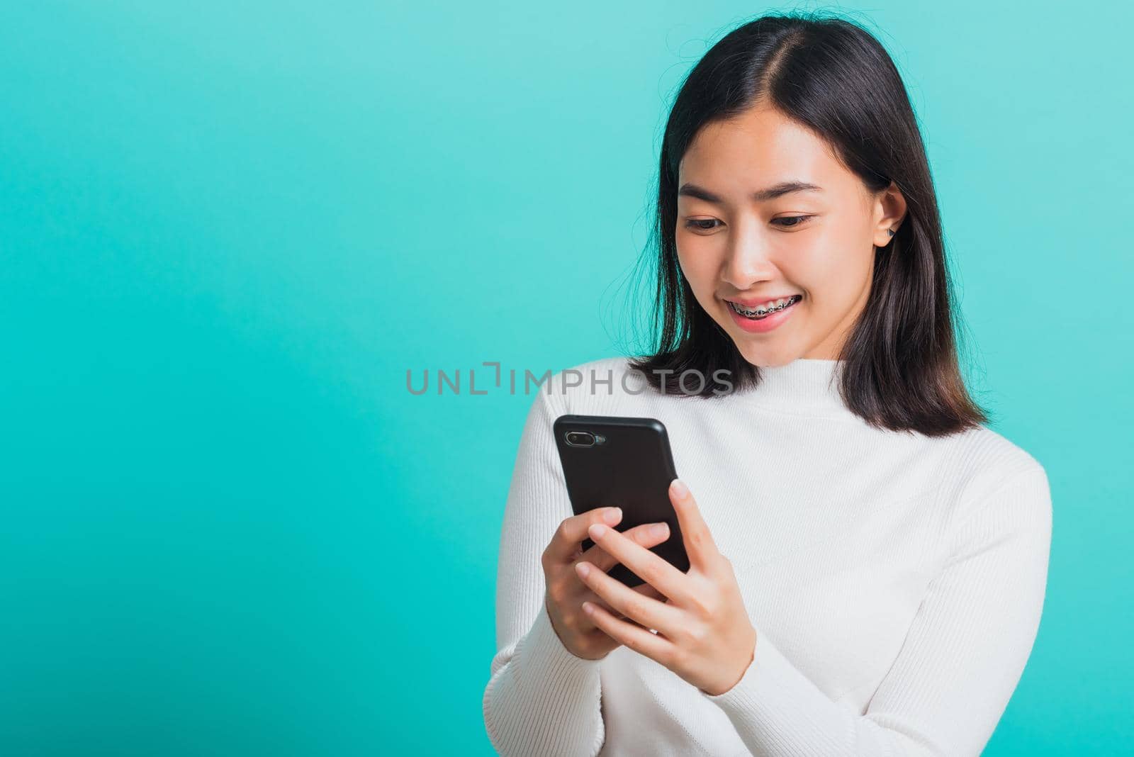 Portrait of Asian woman smile she holding and typing text message on a smartphone, female excited cheerful her reading mobile phone some social media isolated on a blue background, Technology concept