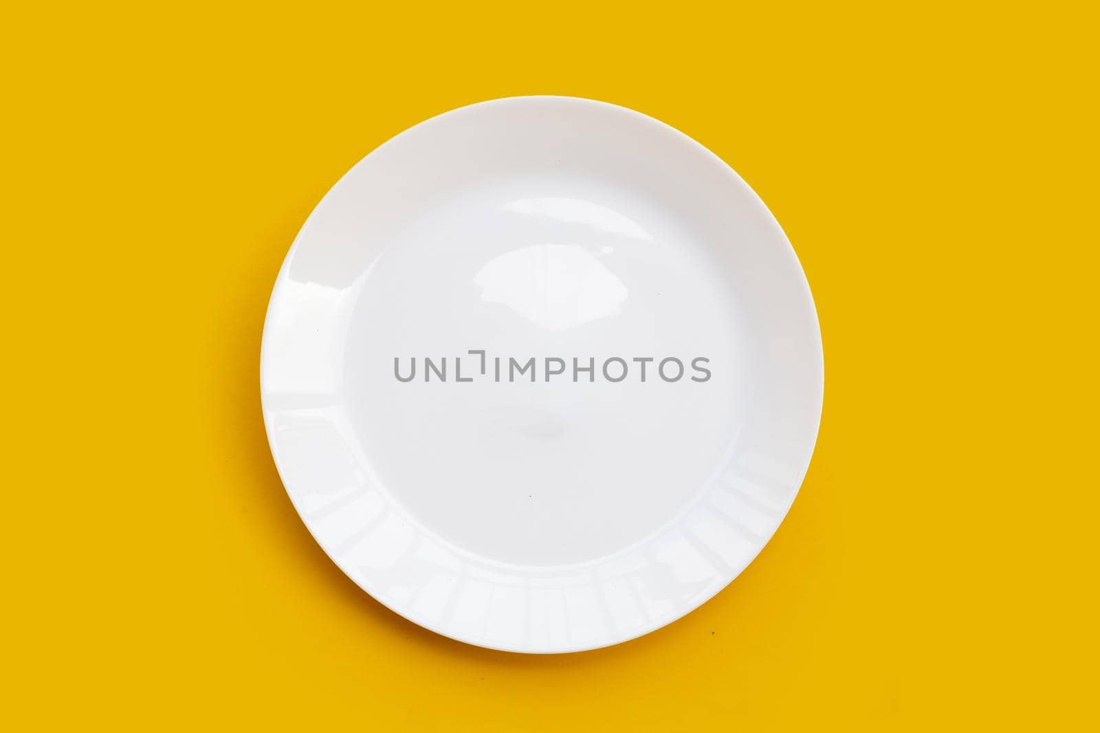 Empty white dish plate on yellow background. 
