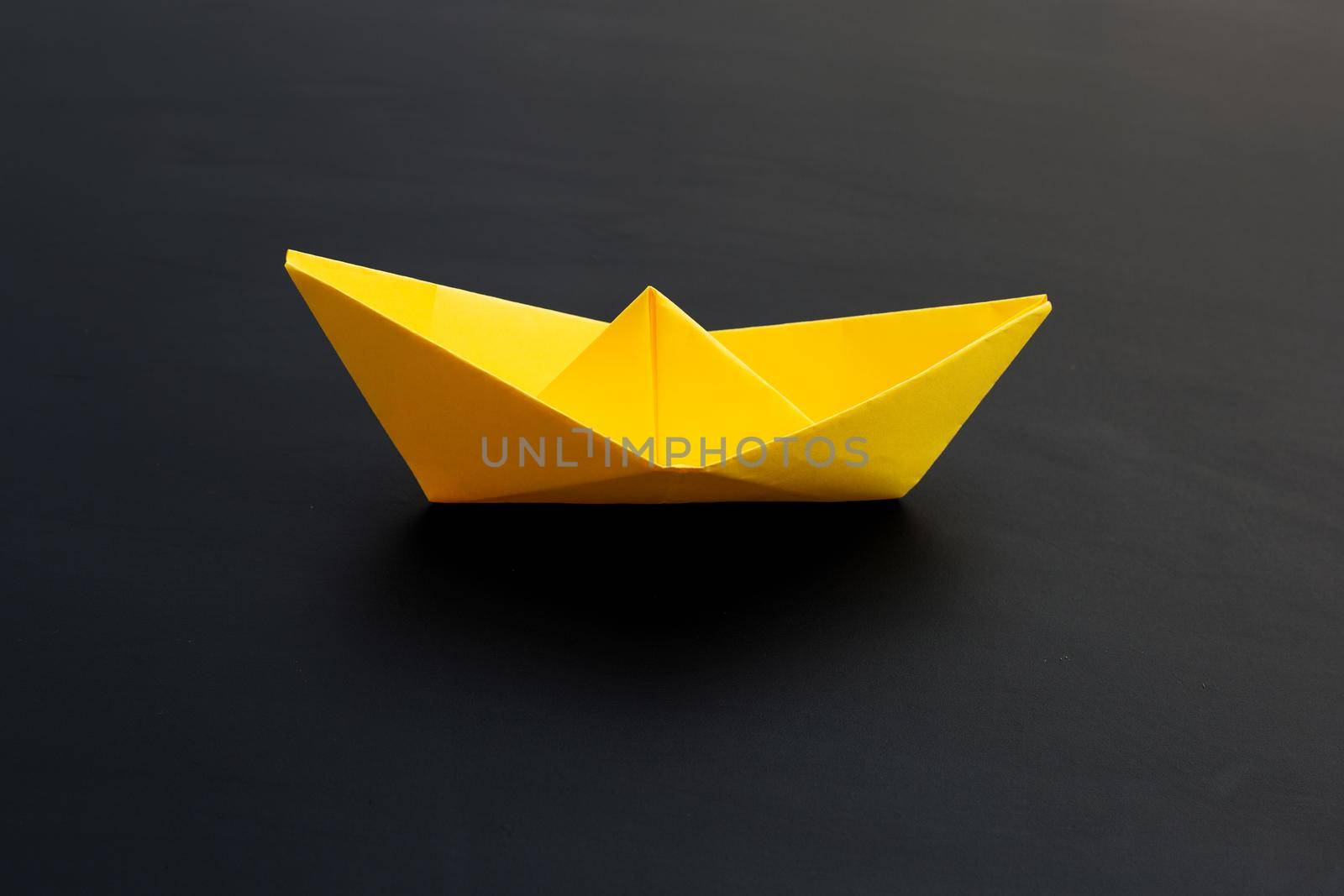 Yellow paper boat on dark background. Copy space