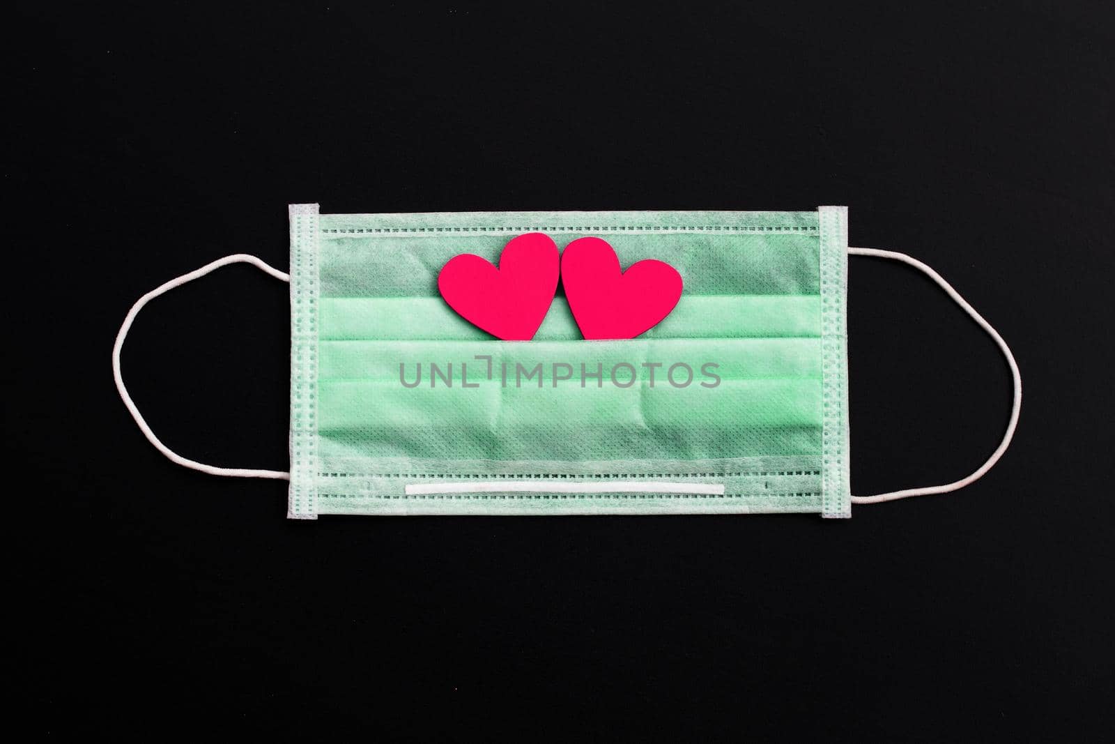 Two pink wooden hearts on protective medical mask on dark background.