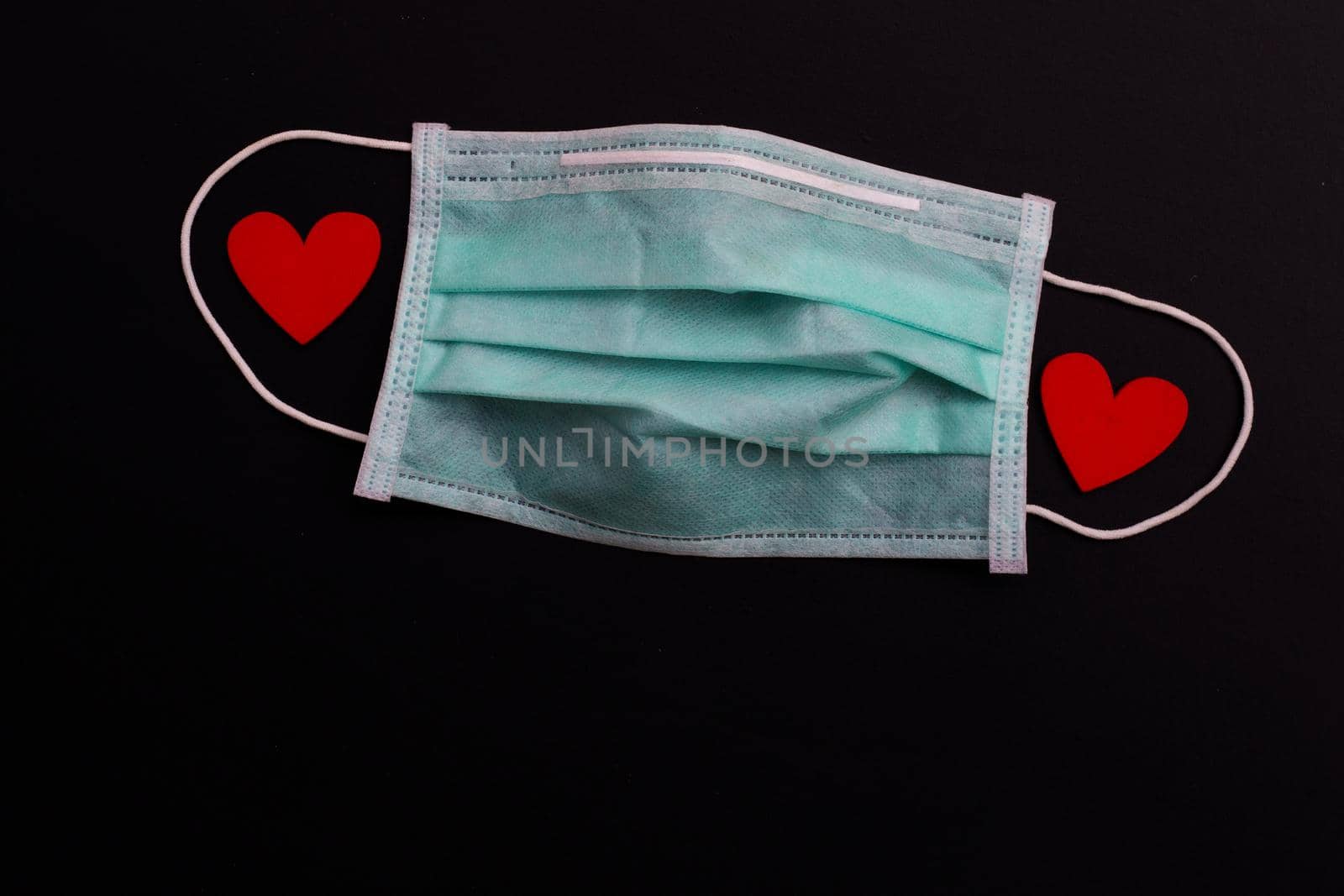Two red wooden hearts on protective medical mask on dark background.