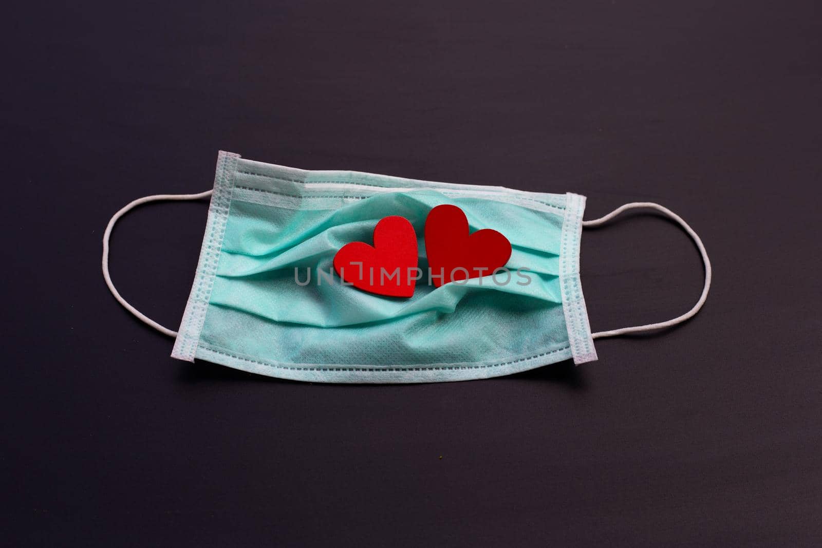 Two red wooden hearts on protective medical mask on dark background.