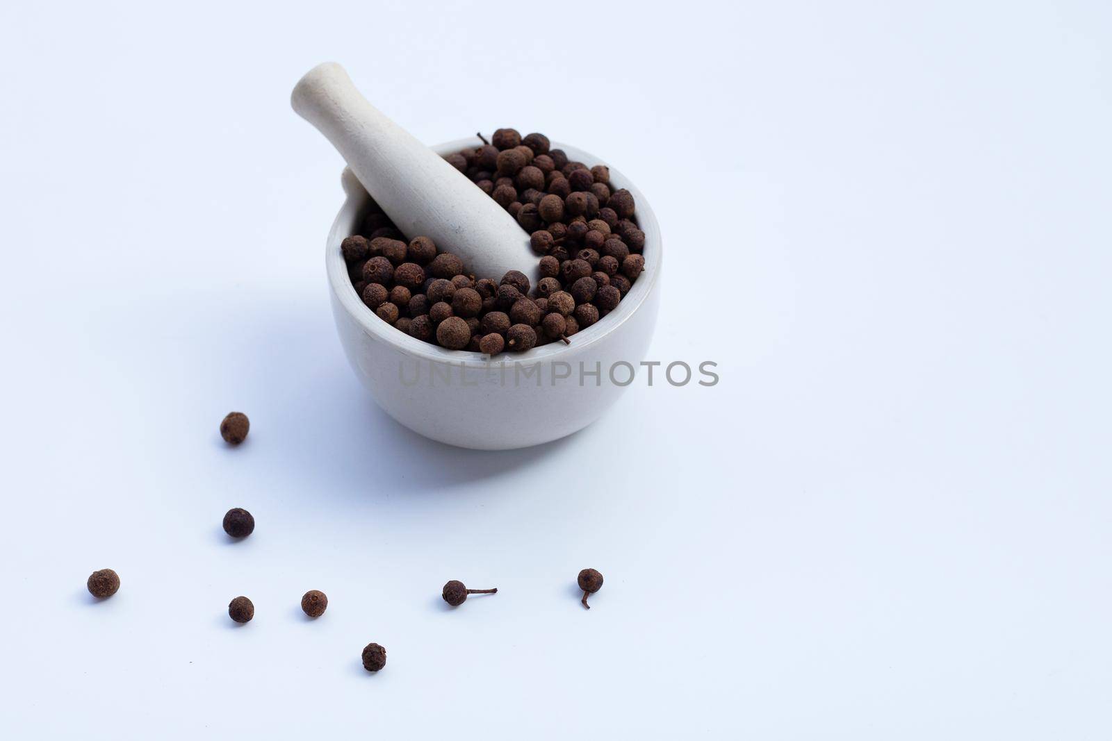 Allspice in porcelain mortar with pestle on white background.
