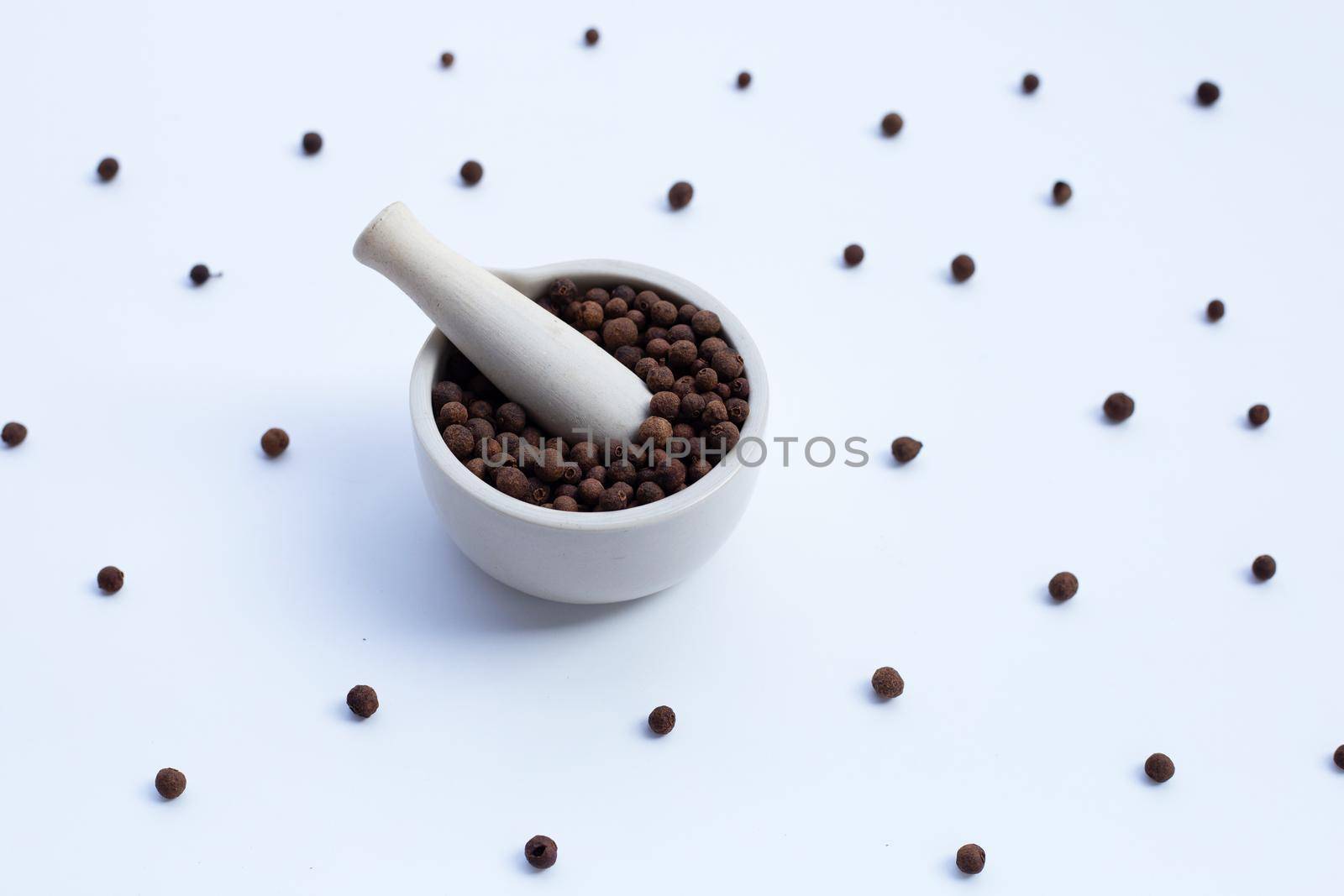 Allspice in porcelain mortar with pestle on white background.