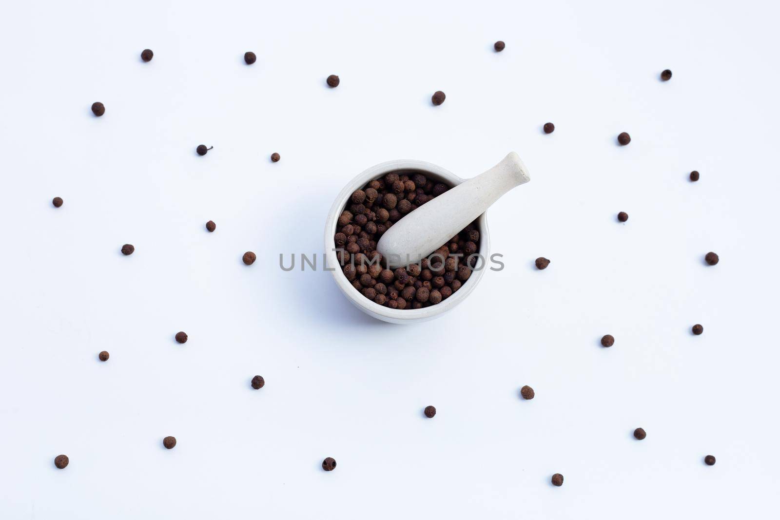 Allspice in porcelain mortar with pestle on white background.