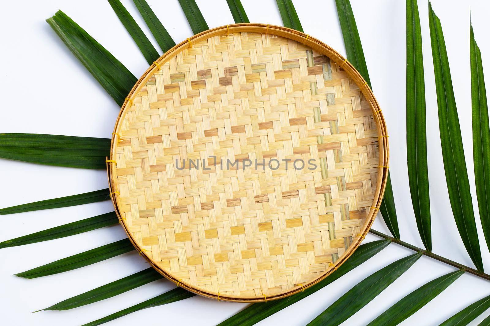 Empty wooden bamboo threshing basket on tropical palm leaves on white background.