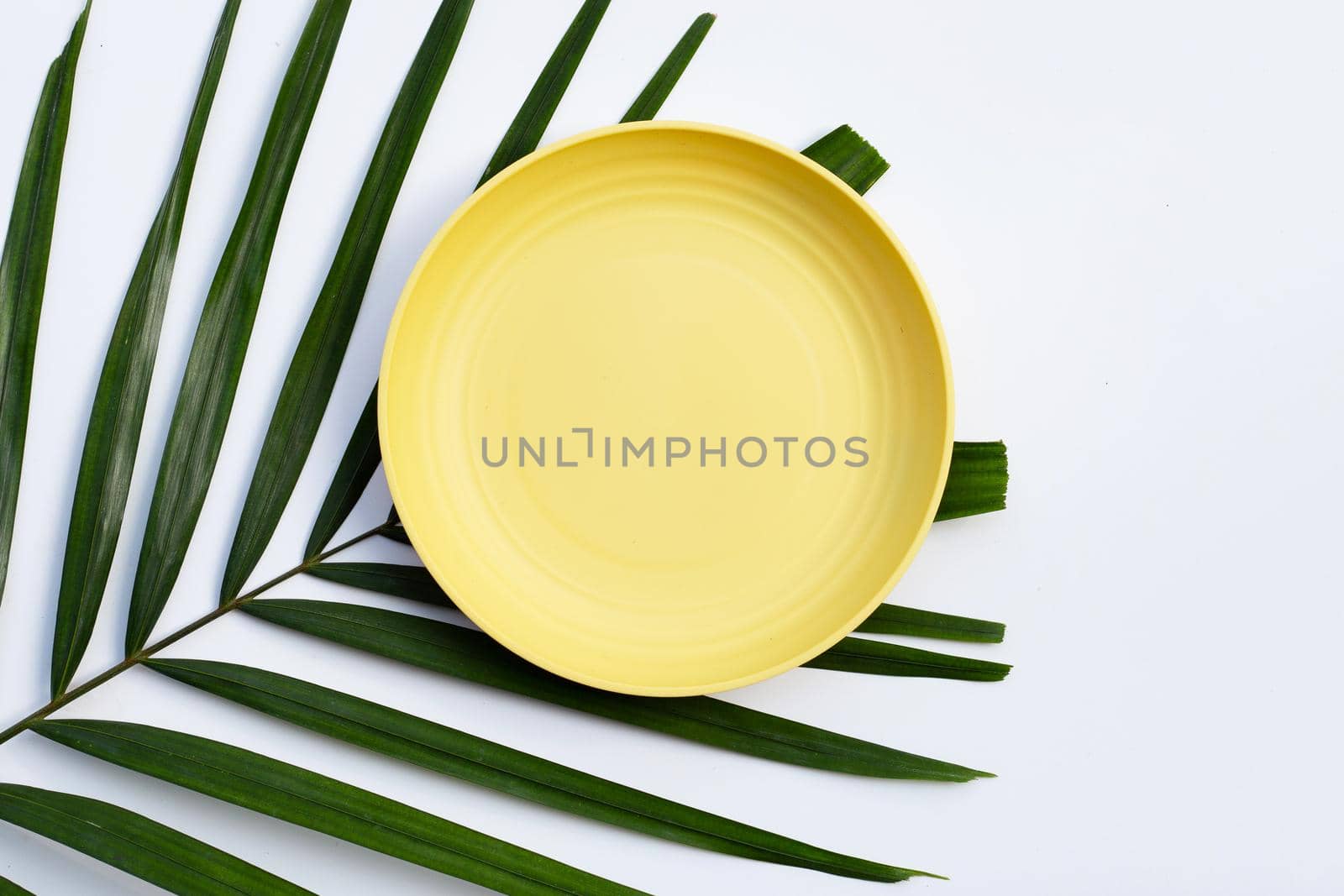 Empty yellow plate on tropical palm leaves on white background. Top view
