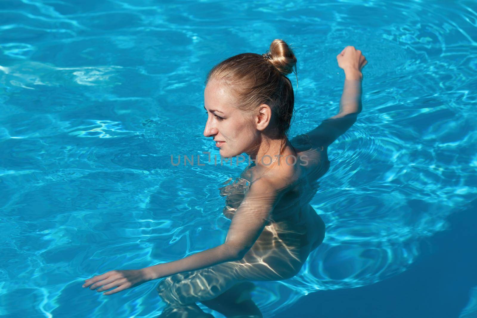 Naked woman outdoors. Beautiful young nude woman in swimming pool. Young nude blonde swims in the outdoor pool