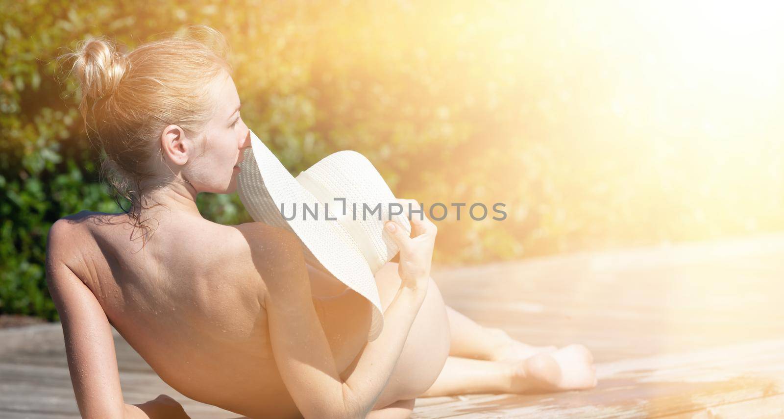 Naked woman outdoors. Beautiful young nude woman in swimming pool. Young nude blonde rests on the wooden side of the outdoor pool by the sea