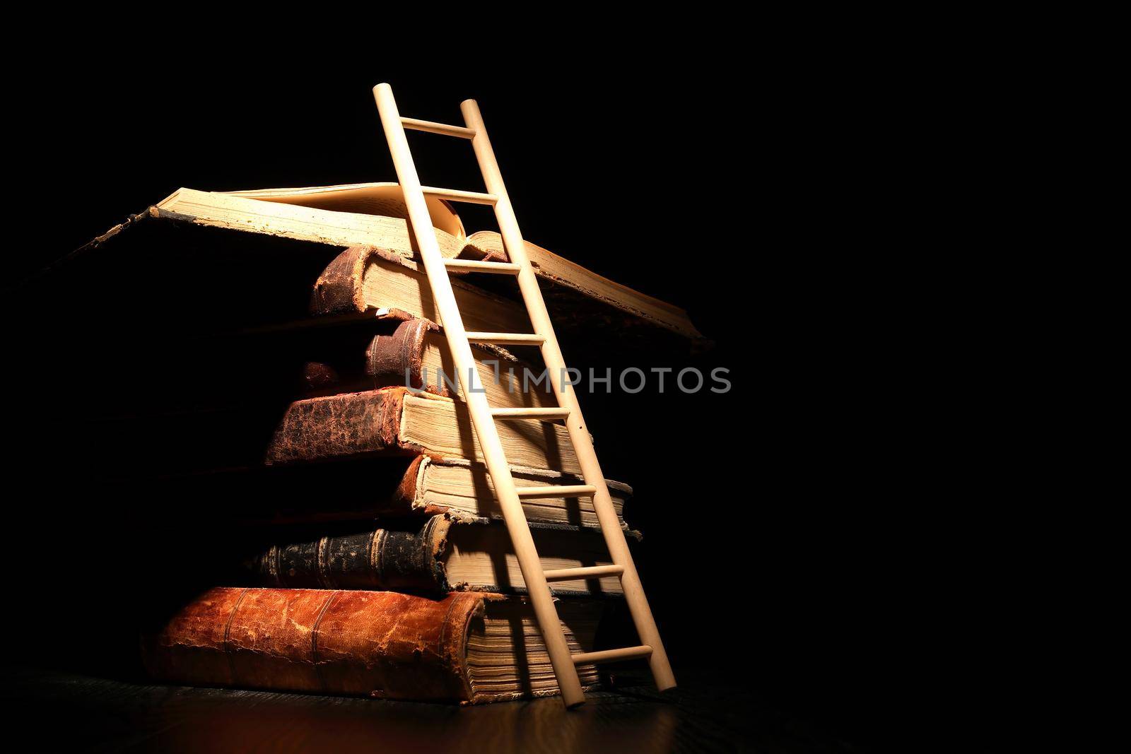 Education concept. Stack of old books and ladder on dark background