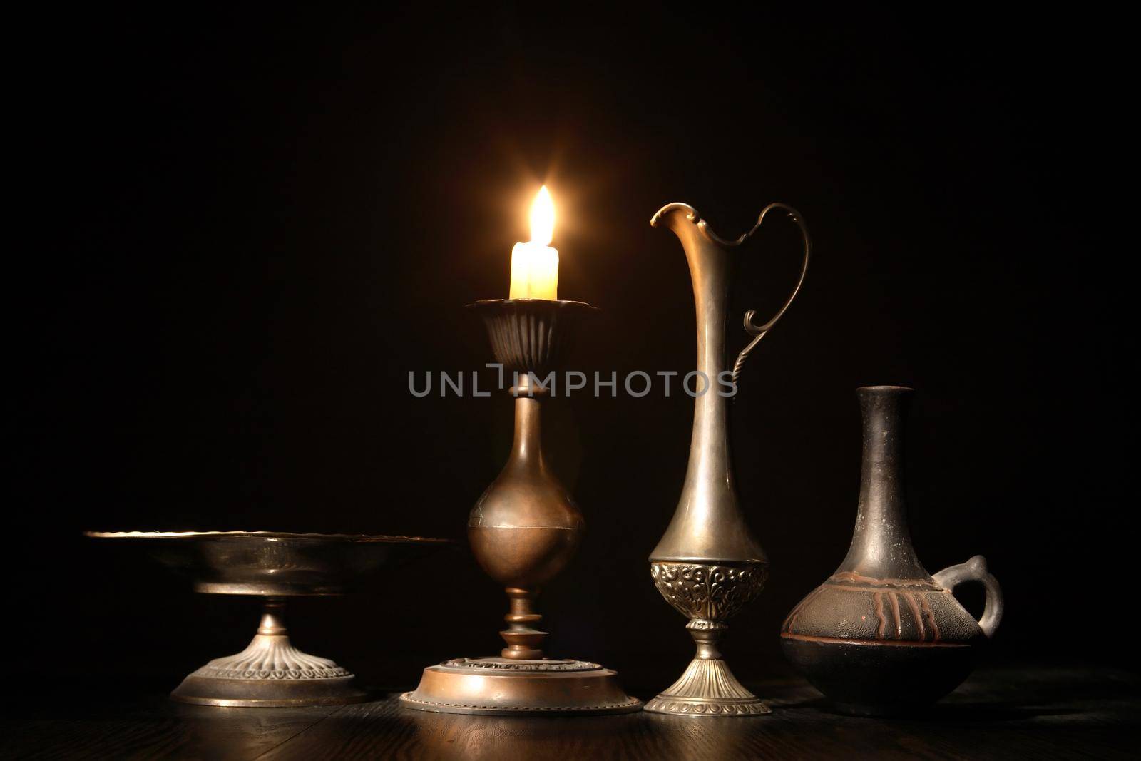 Set of vintage dishes near lighting candle on dark background