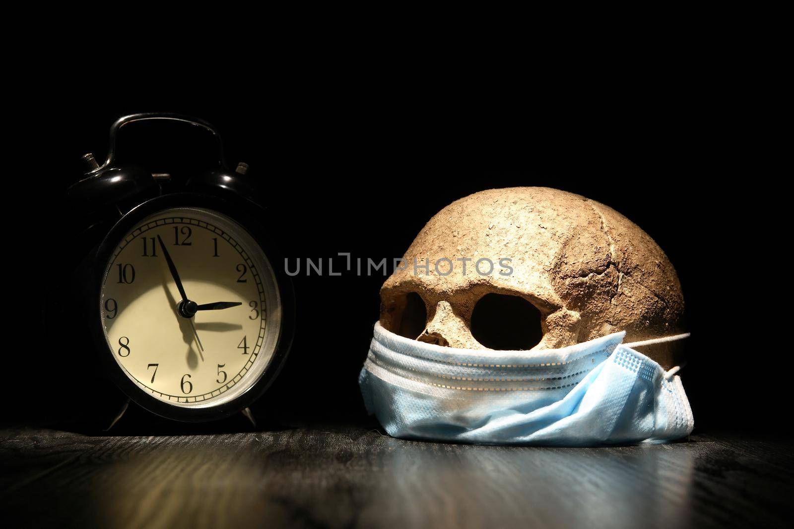 Covid concept. Human skull in medical mask near alarm clock
