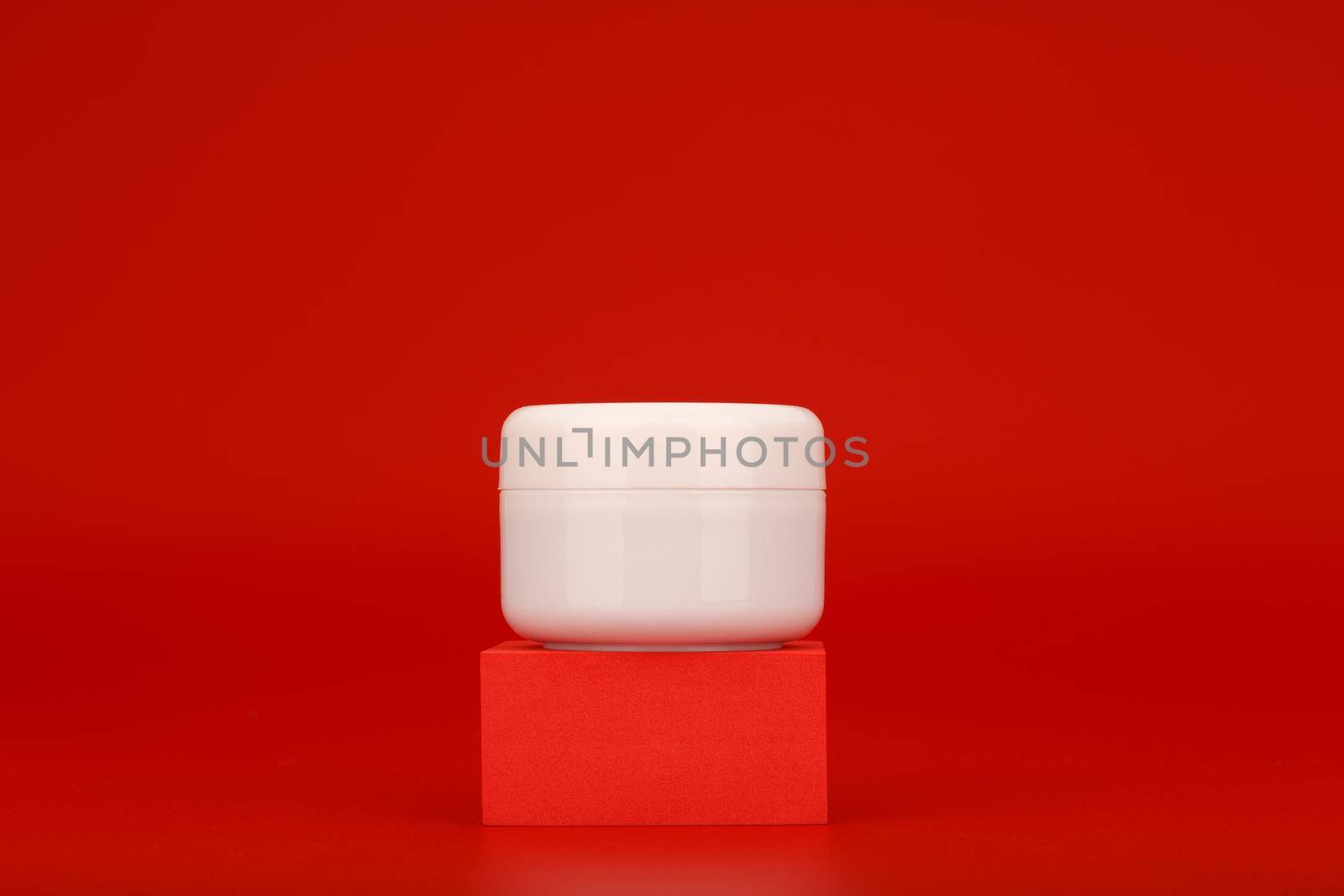 White cosmetic jar with cream, mask or scrub on red podium against red background with copy space. Concept of beauty routine and skin care or hair care