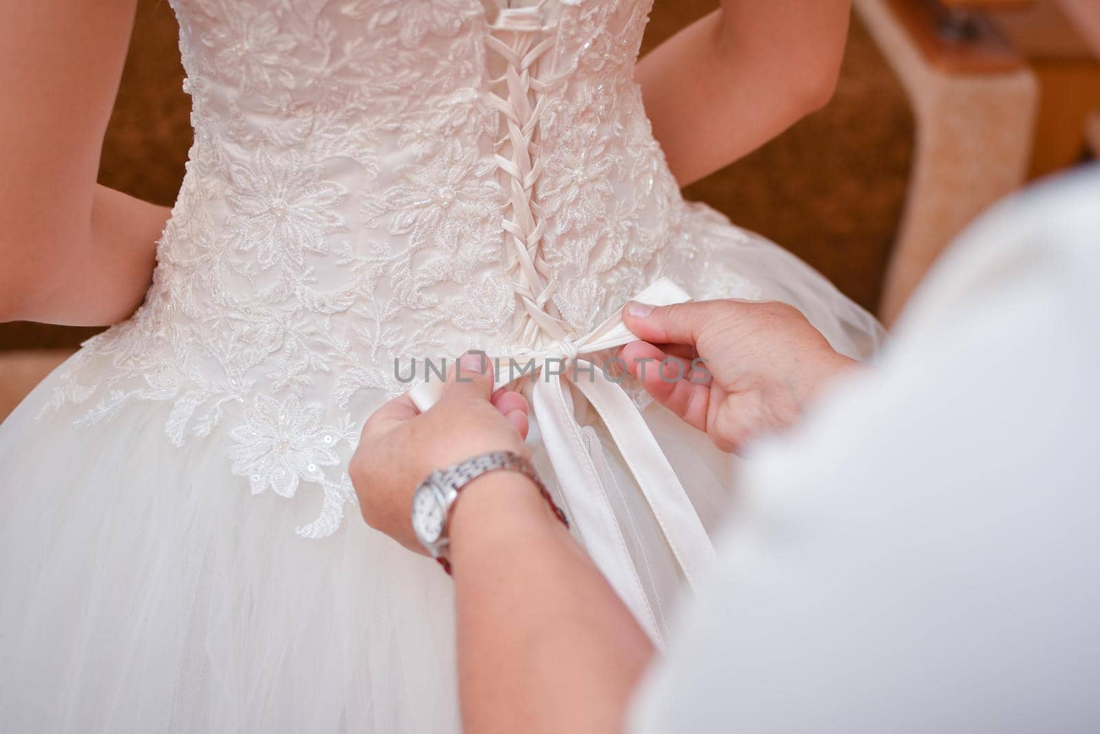 Wedding dress, corset. Mom ties a bow on the bride's dress. Rear view.