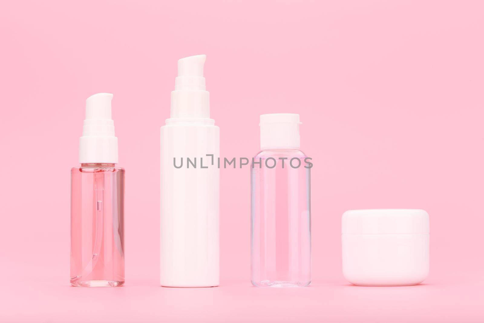 Minimalistic still life with set of unbranded cosmetic bottles with cleansing gel, face cream, lotion and under eye cream against bright pink background