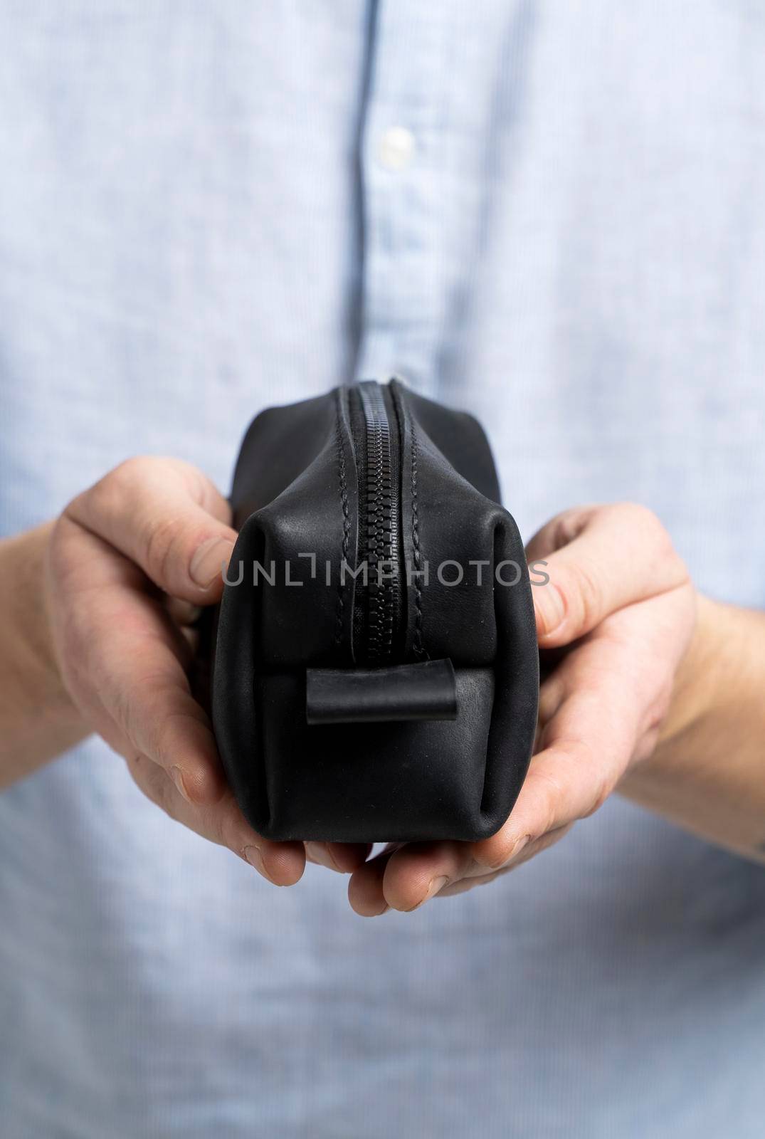 Man's black leather personal cosmetic bag or pouch for toiletry accessory in a men's hands in blue shirt. Style, retro, fashion, vintage and elegance