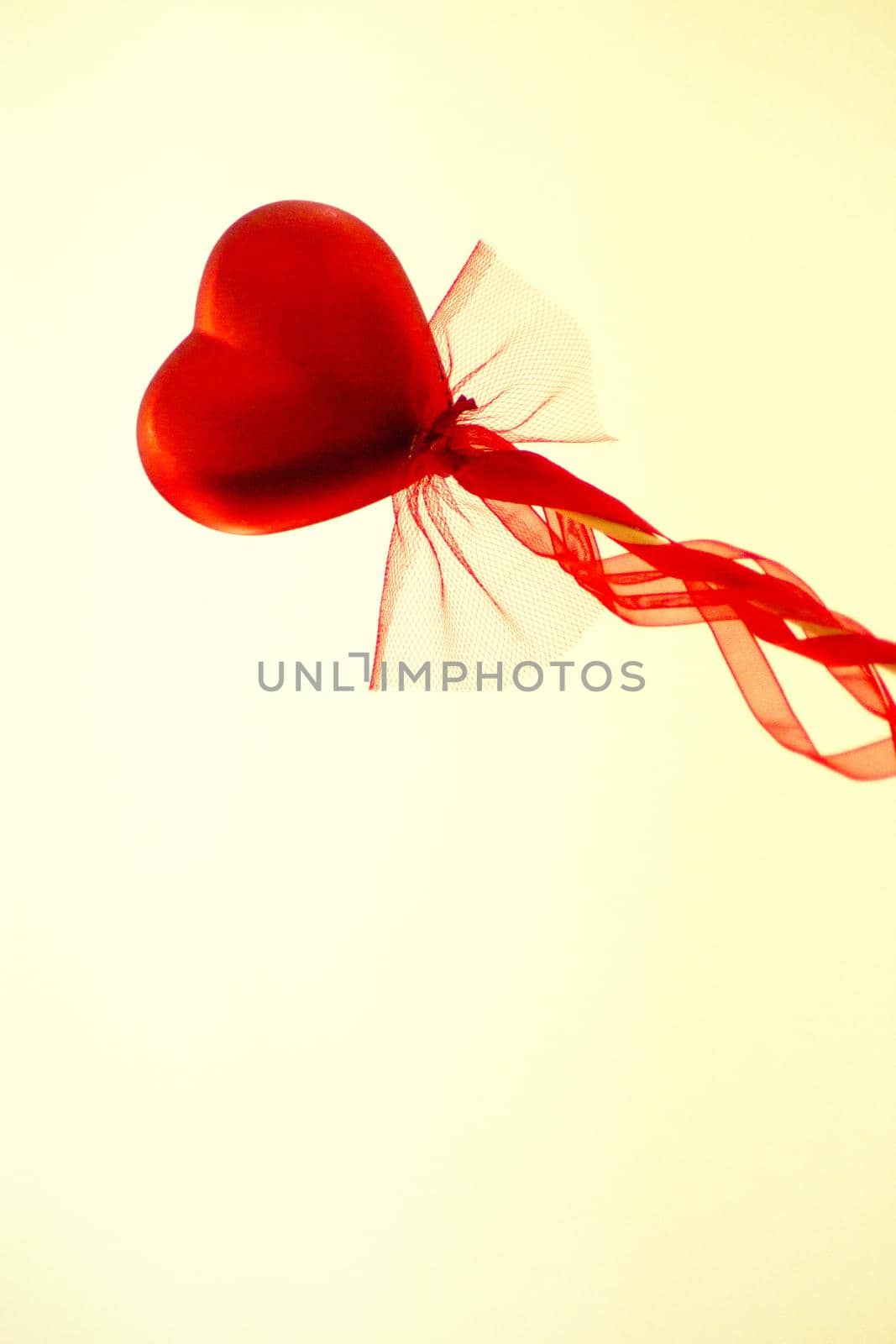 Red heart attached to a stick with a bow hanging. Copy space