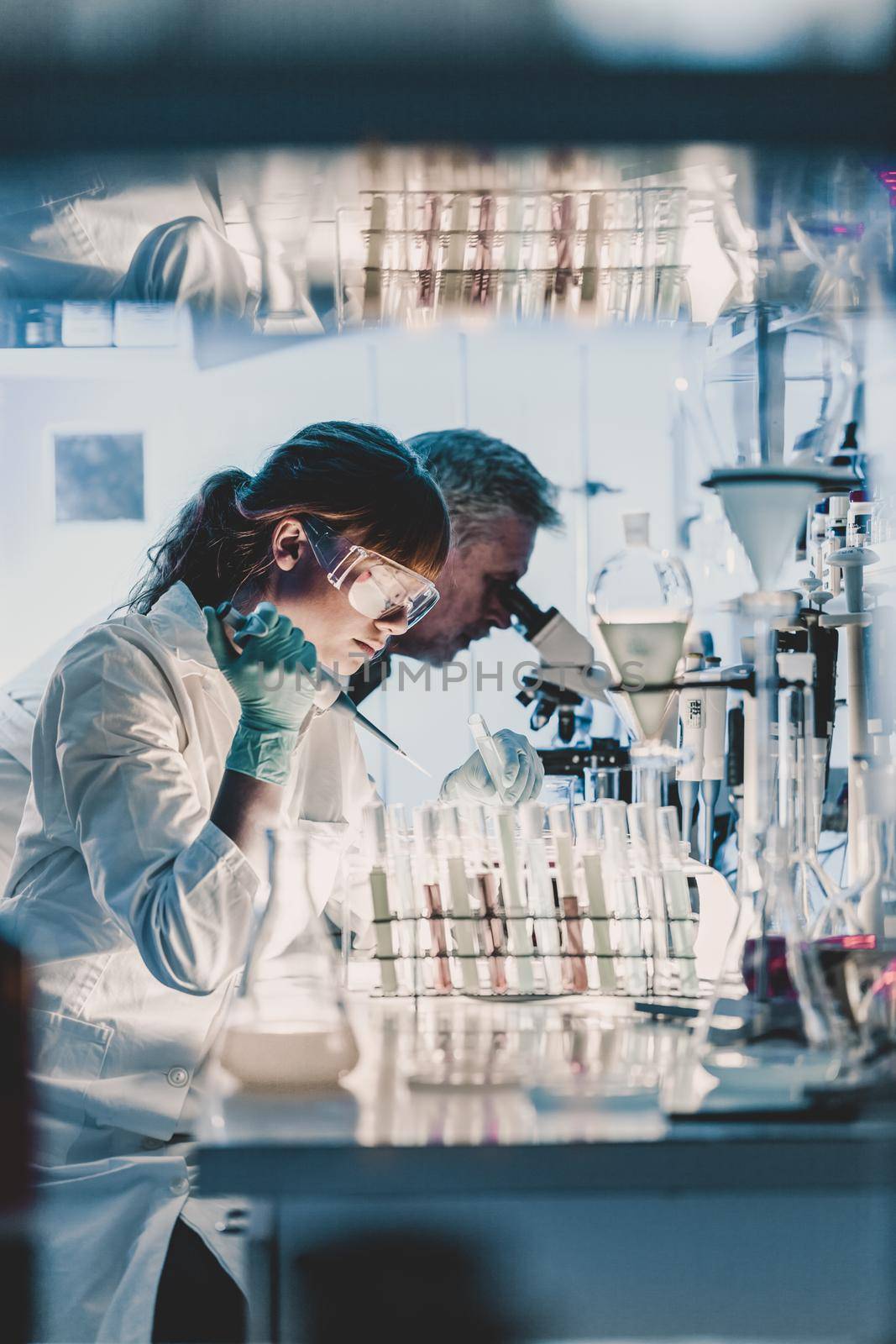 Health care researchers working in life science laboratory. Young female research scientist and senior male supervisor preparing and analyzing microscope slides in research lab.
