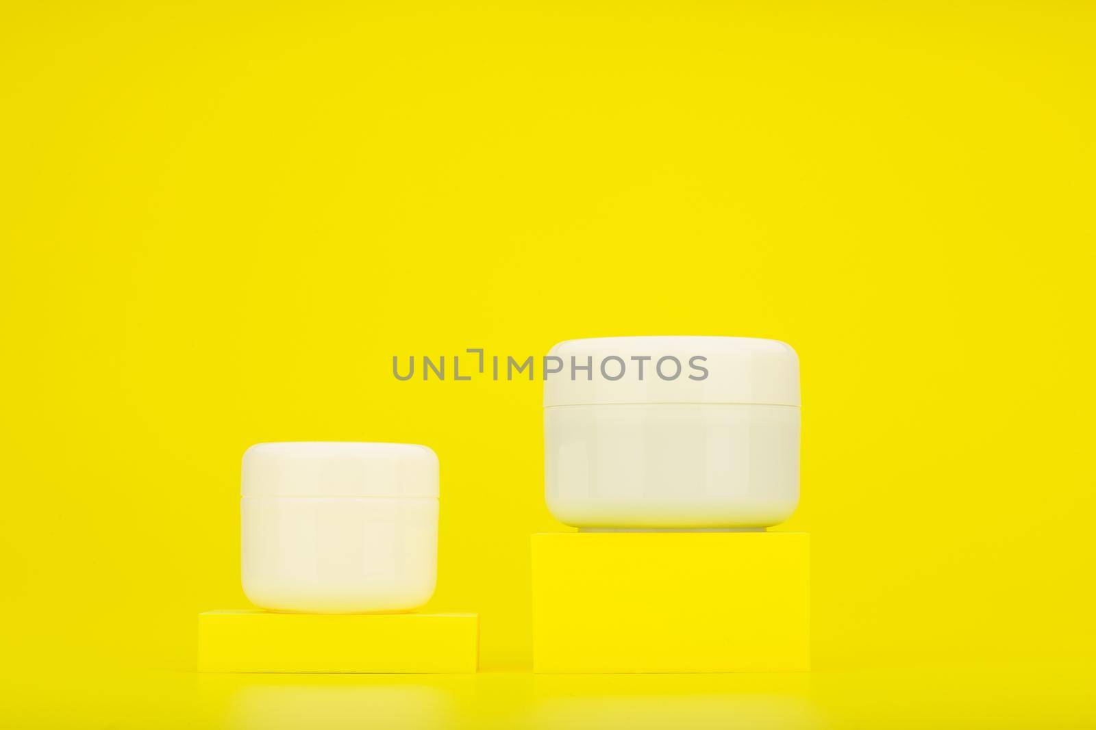 Two unbranded cosmetic jars on yellow podiums against bright yellow background with copy space by Senorina_Irina