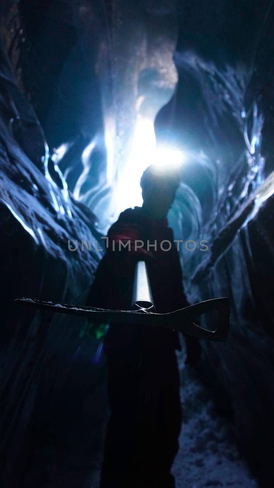 A climber with an ice pick stands at exit of cave by Passcal