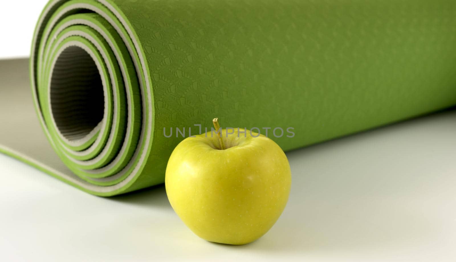 Yoga fitness, health life style. Yoga rolled green mat and green apple on white background. Place for text. Healthy lifestyle, fitness, sport concept