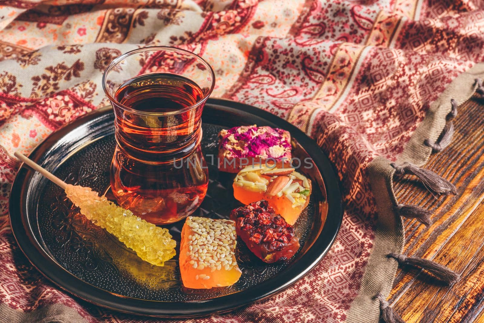 Tea in armudu glass with oriental delight rahat lokum on metal tray over wooden surface and tablecloth