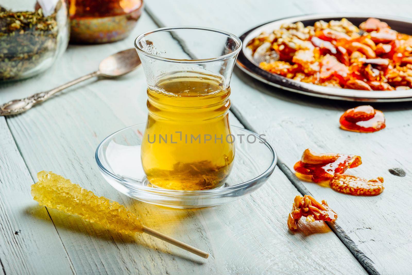 Green tea in armudu glass with oriental nut delights on metal plate over light wooden surface