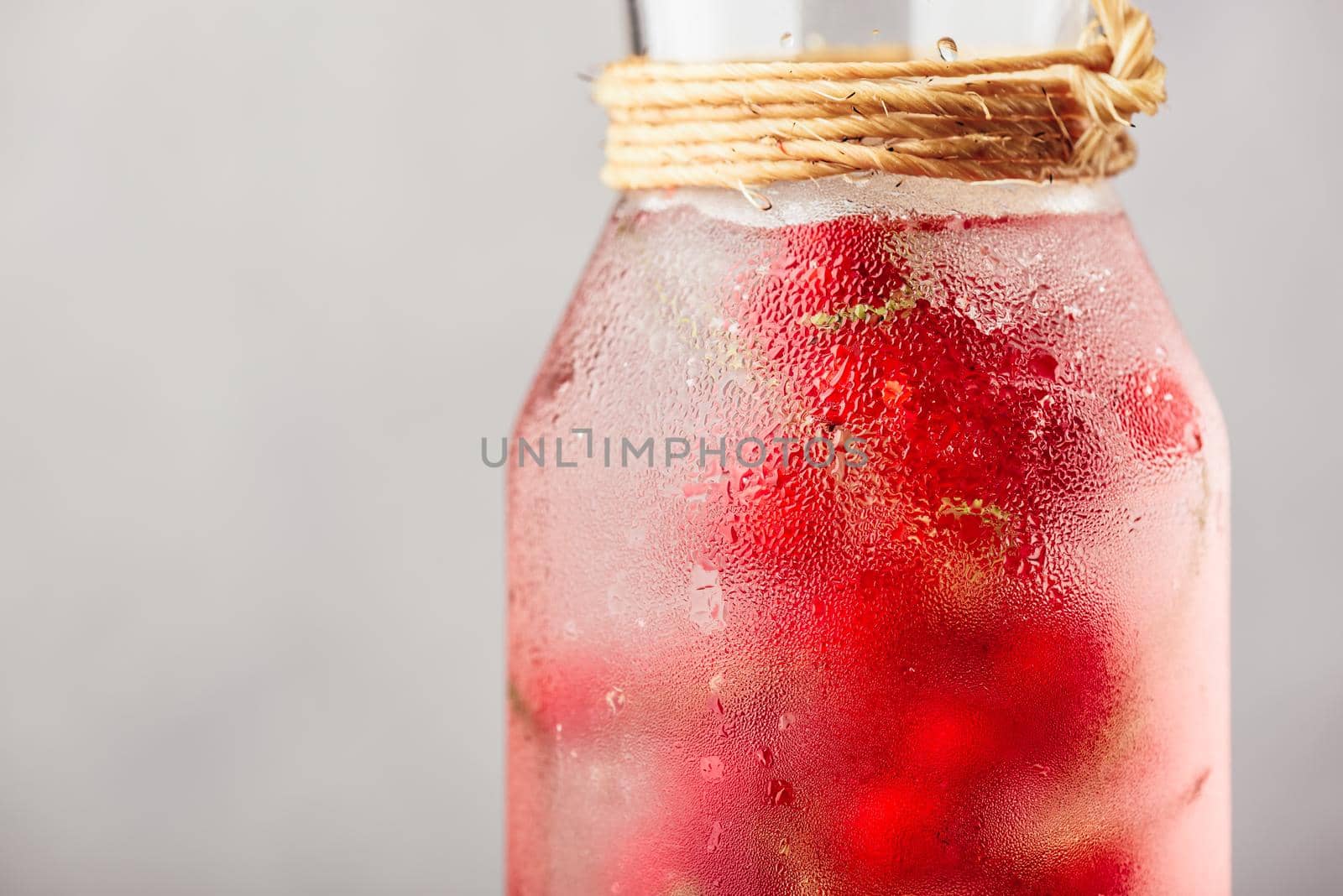 Red currant infused water with ice in glass bottle