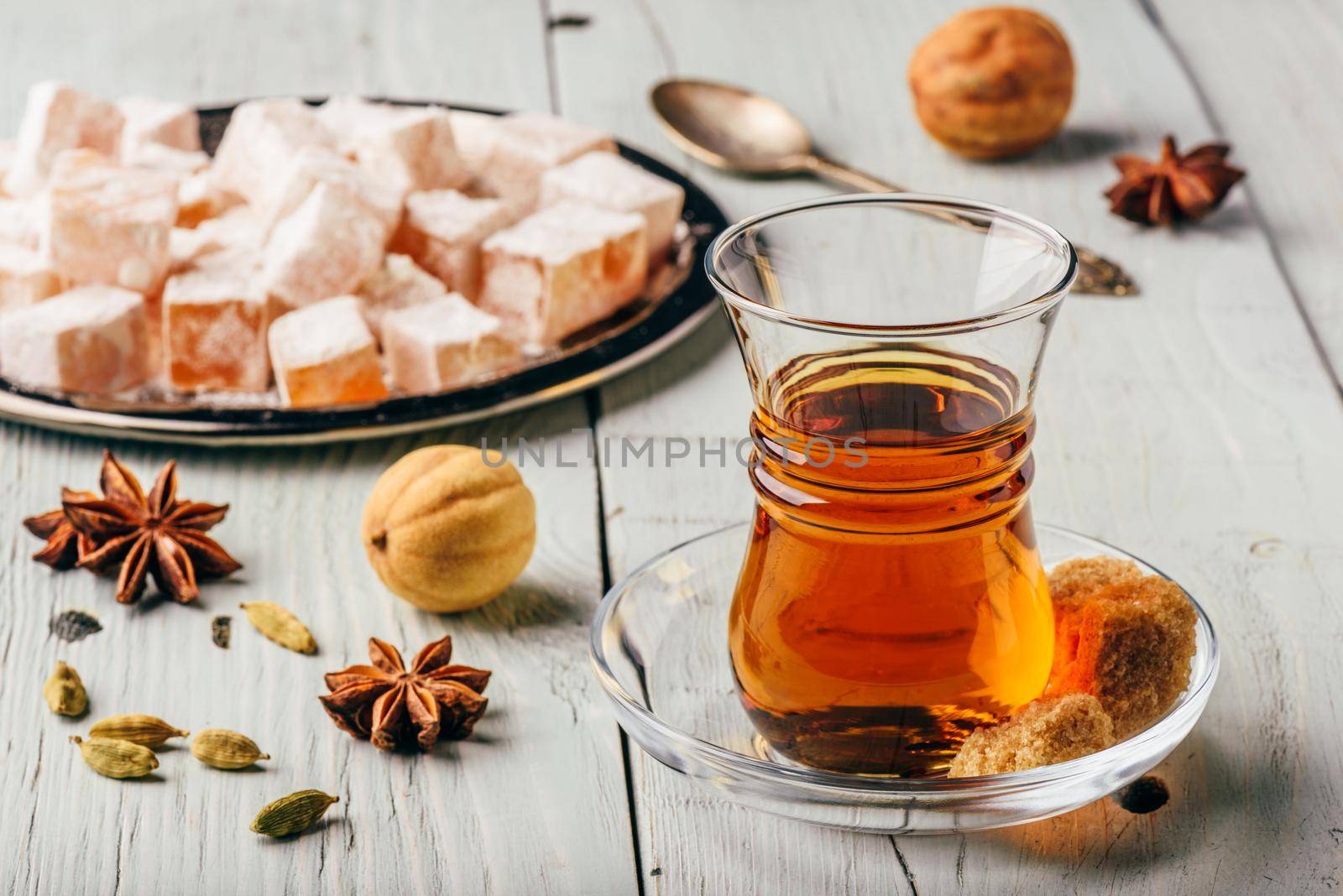 Tea in arab glass with turkish delight Rahat Lokum and different spices over wooden surface