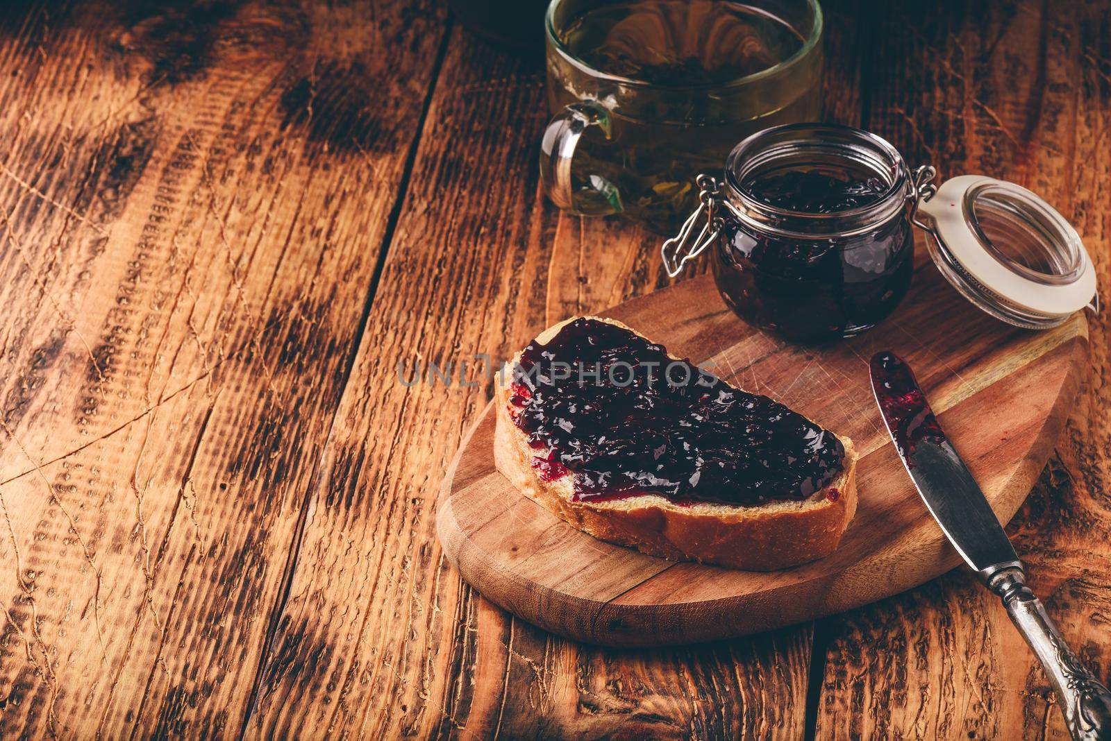 Toast with berry jam on cutting board and cup of green tea in rustic setting