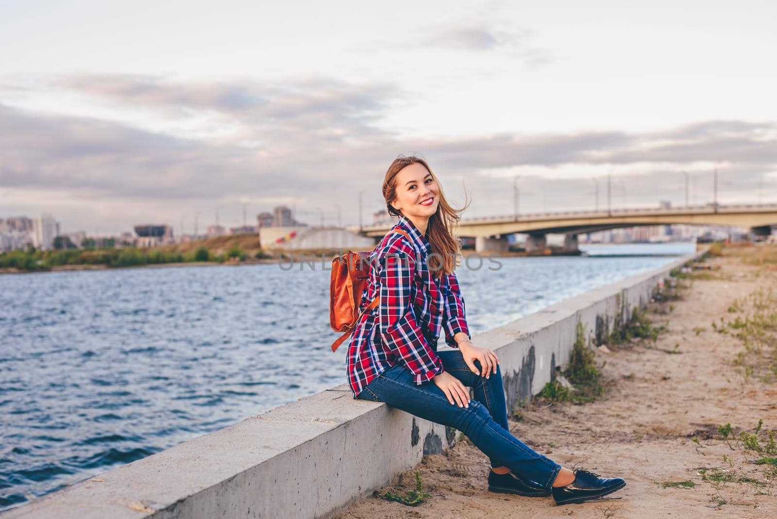 Smiling woman sitting on the riverbank during summer sunset