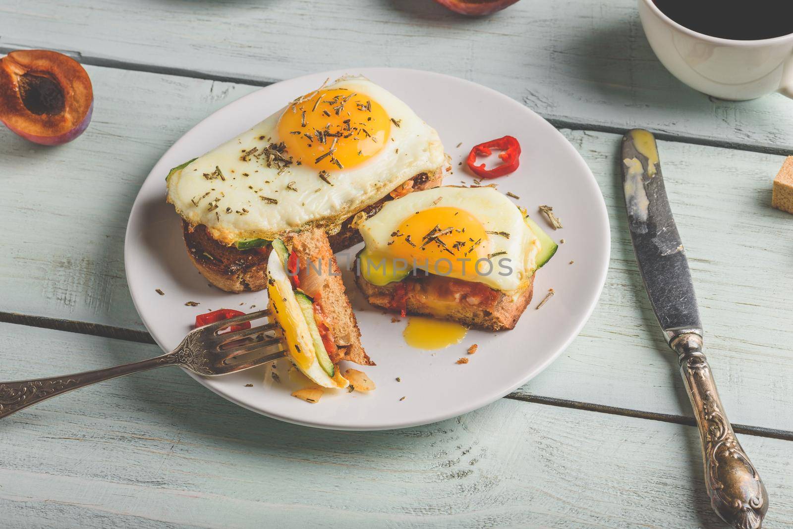 Breakfast toasts with vegetables and fried egg on white plate, cup of coffee and some fruits over wooden background. Clean eating food concept.