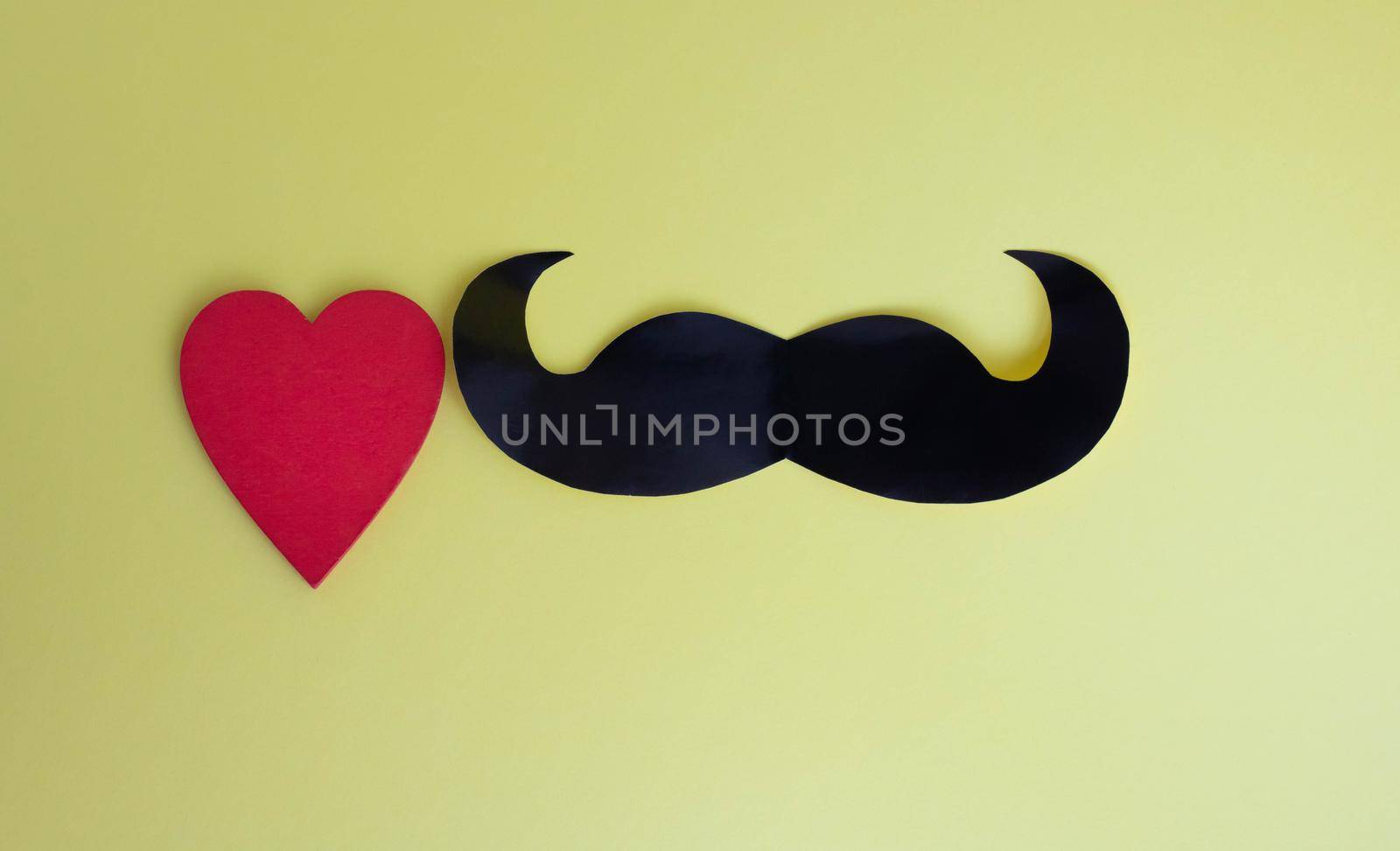 Father's Day concept. Black mustache and red heart on a yellow paper background.