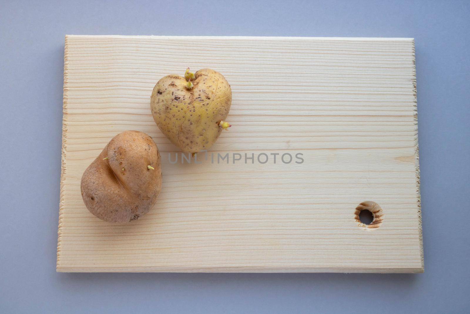 Two unusual heart-shaped potatoes with sprouts lie on a wooden board on the table.